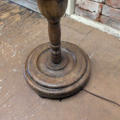 Wooden floor lamp base on a wooden floor with a stone wall in the background