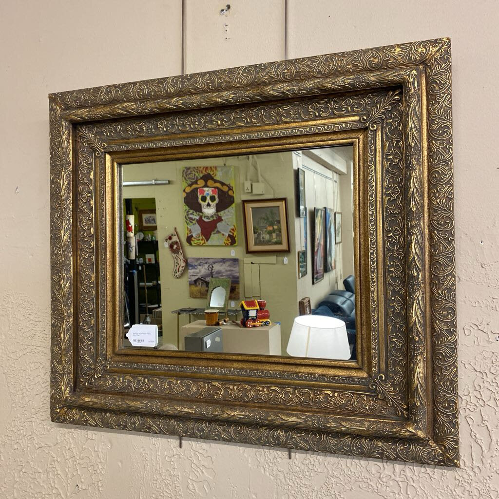 Decorative gold-framed mirror on a textured wall