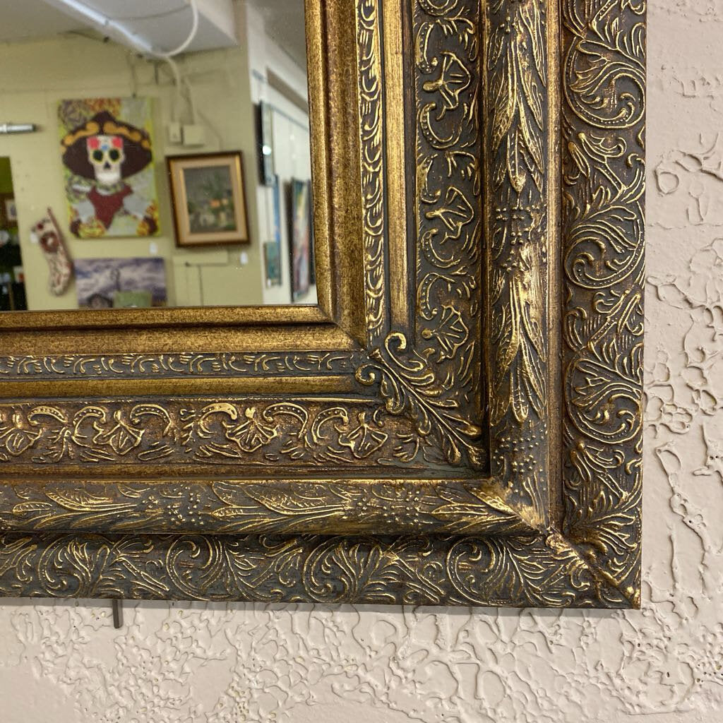 Close-up of an ornate gold mirror frame on a textured wall.