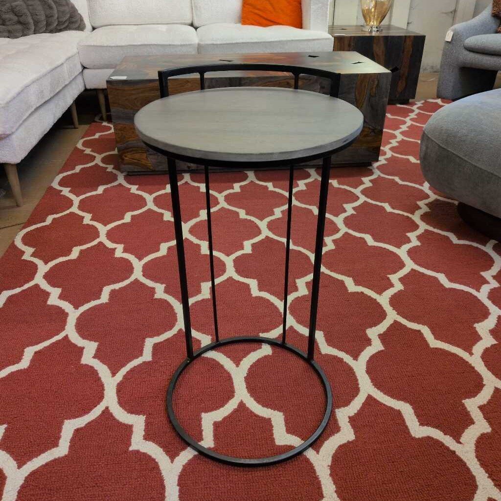 Round metal table with a gray top on a red patterned rug in a living room setting.