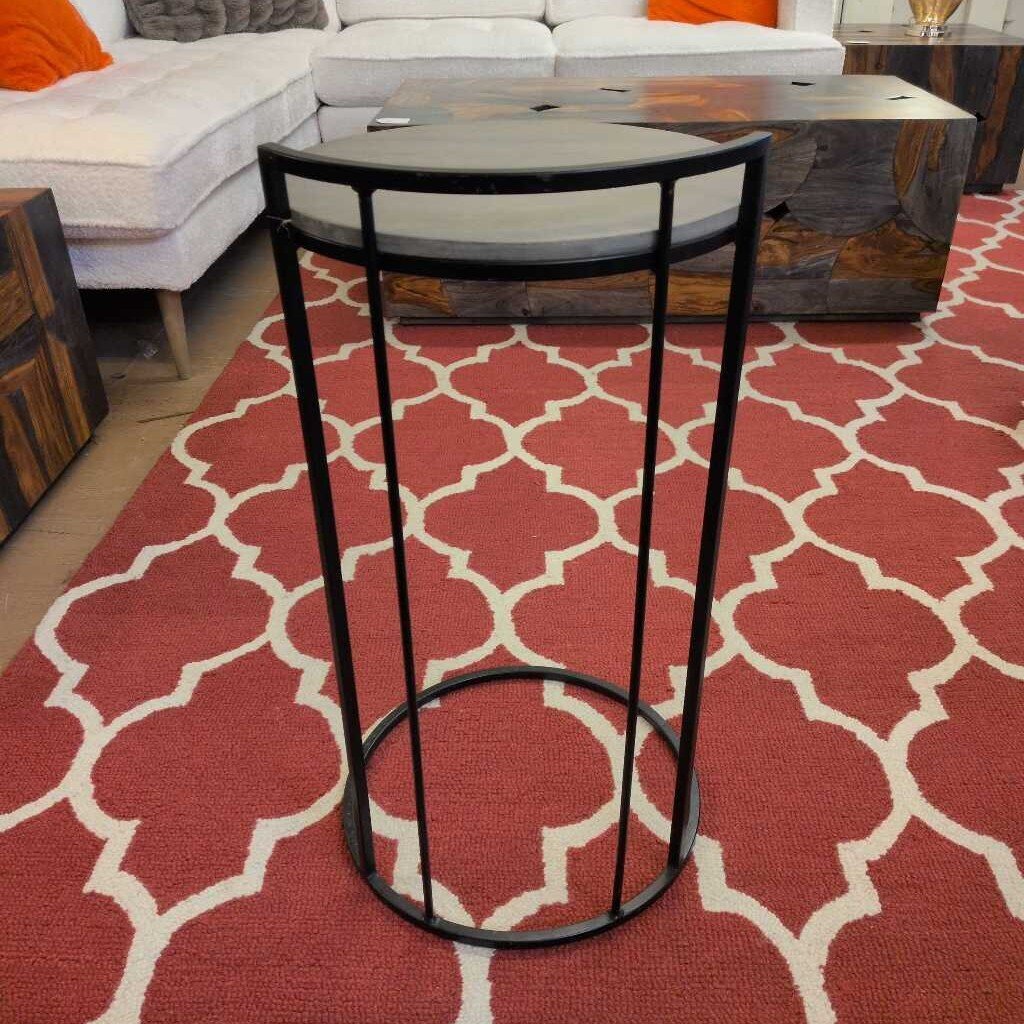 Black metal stool on a red and white patterned rug with a couch in the background
