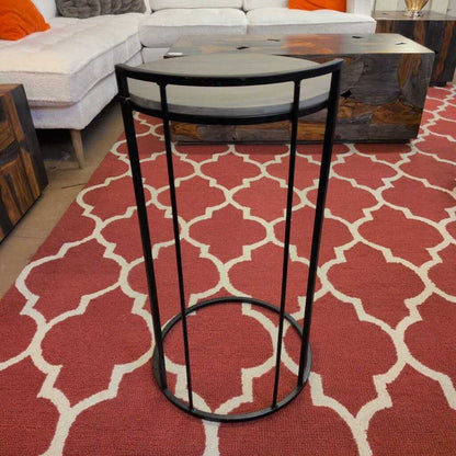 Black metal stool on a red and white patterned rug with a couch in the background