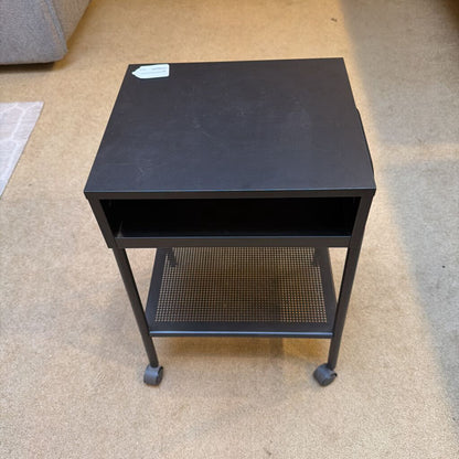 Black metal side table with wheels on a beige carpeted floor