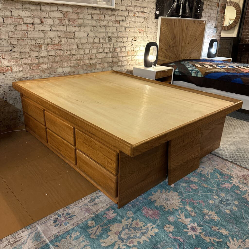 Wooden bed frame with storage drawers in a room with brick wall and rug.