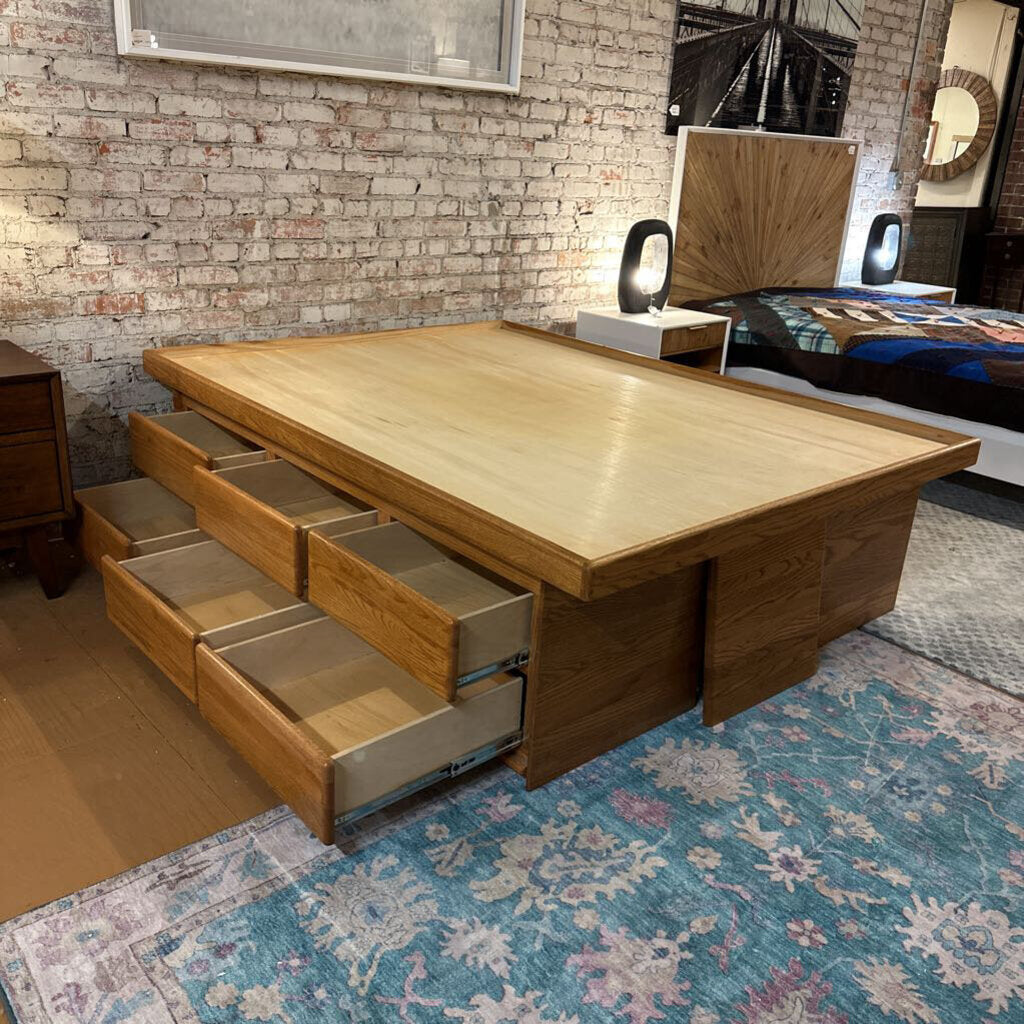 Wooden bed with storage drawers in a room with brick walls and a rug.