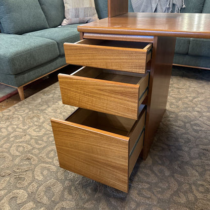 Wooden desk with open drawers in a room with a gray sofa and patterned carpet.