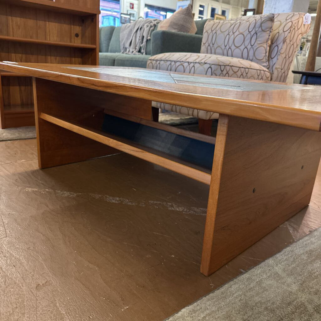 Wooden coffee table in a furniture store setting with a couch and bookshelf in the background.