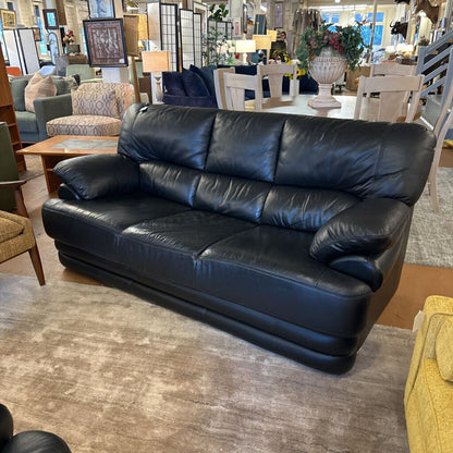 Black leather sofa in a furniture store setting with various other items in the background.