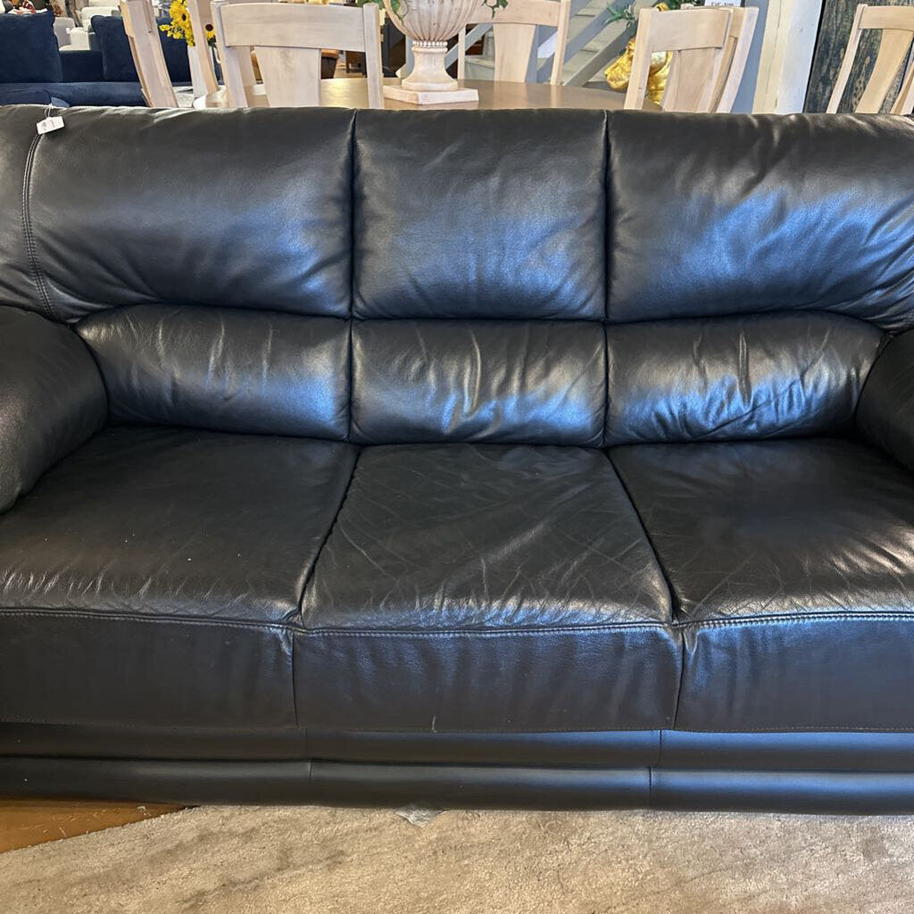 Black leather sofa in a room with chairs and a table.