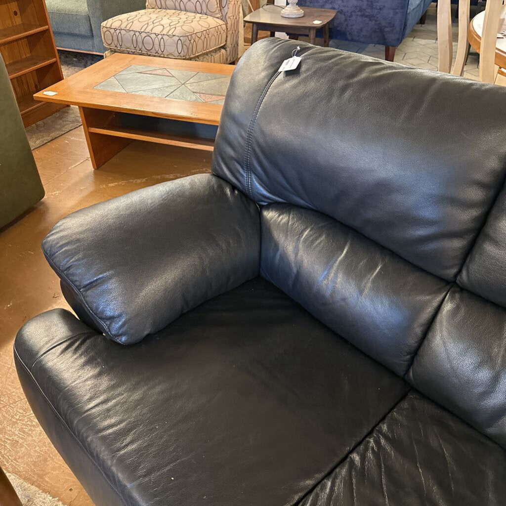 Black leather sofa in a room with wooden furniture and a rug.
