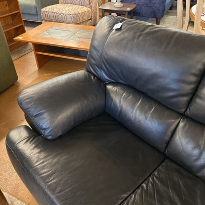 Black leather sofa in a room with wooden furniture and a rug.