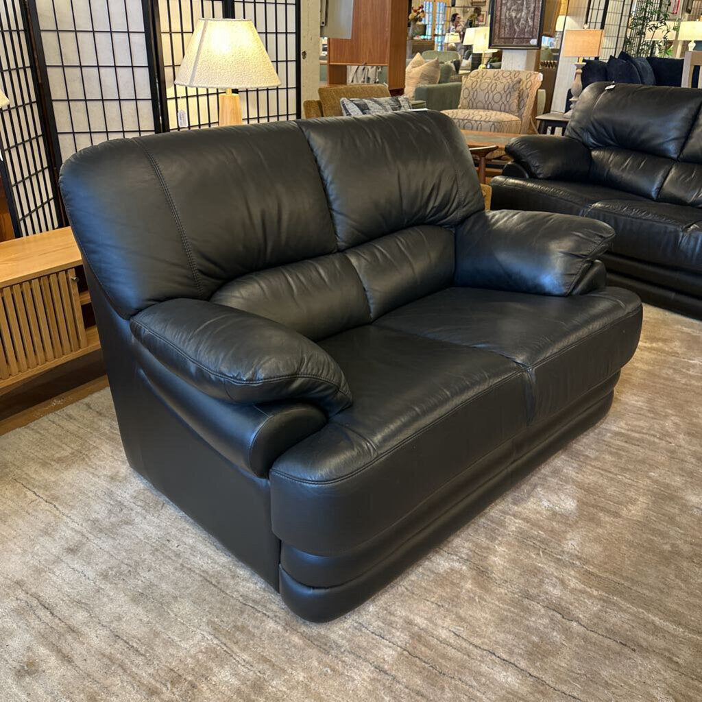 Black leather sofa in a showroom setting with other furniture.