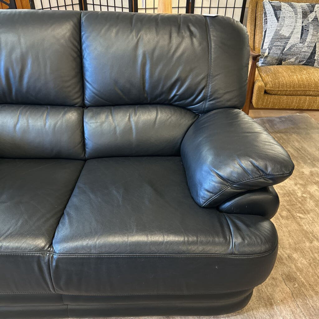 Black leather sectional sofa in a room with a patterned rug and another sofa in the background.