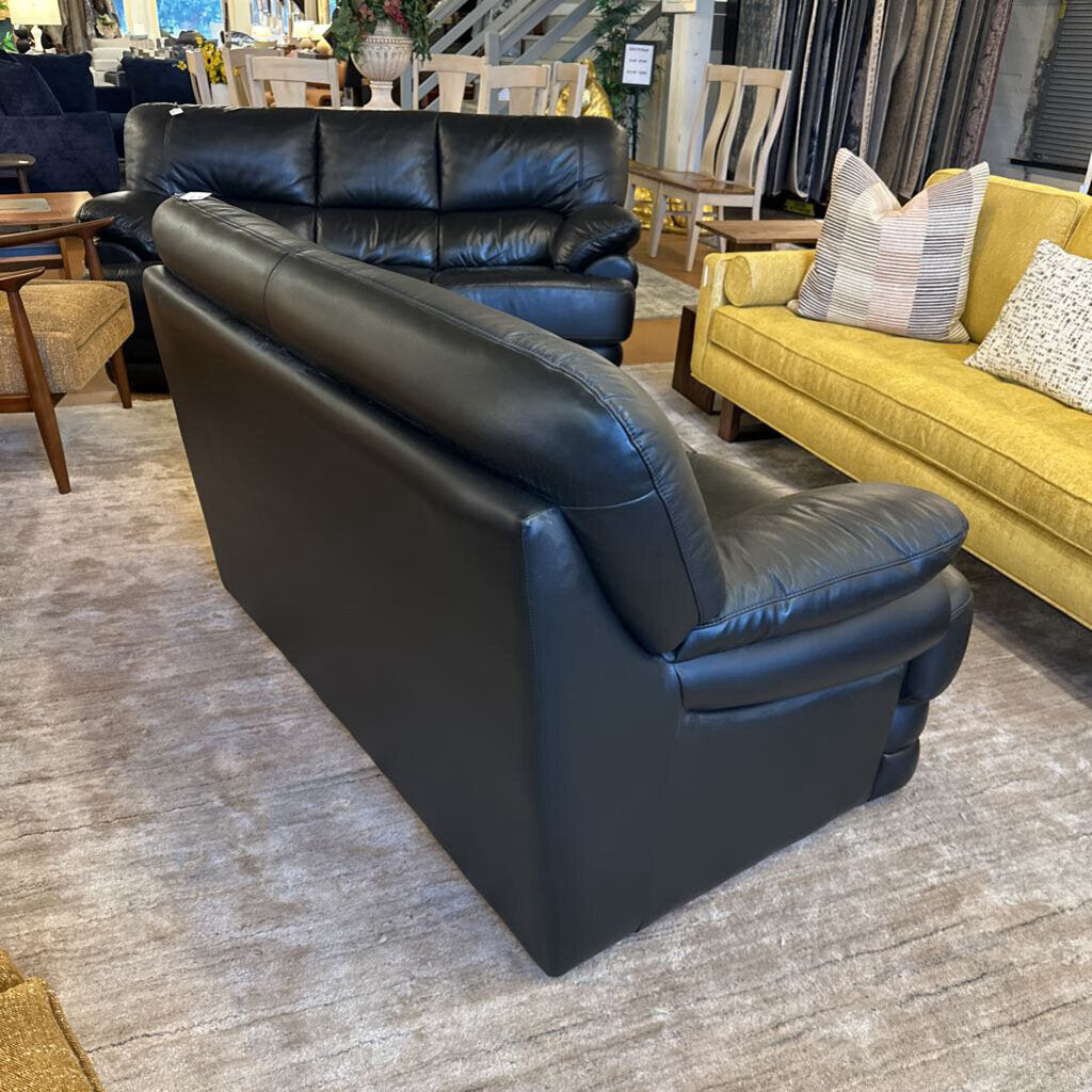 Black leather sofa in a furniture store with yellow couch and striped pillow in the background.