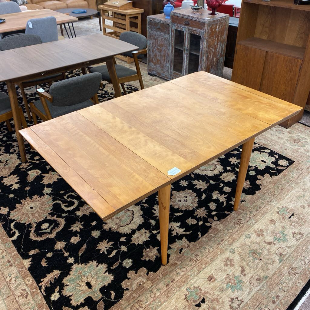 Wooden dining table on a patterned rug with chairs and furniture in the background