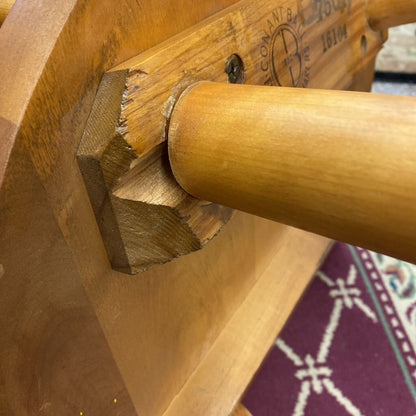 Close-up of a wooden chair arm with a visible brand logo on a textured surface.