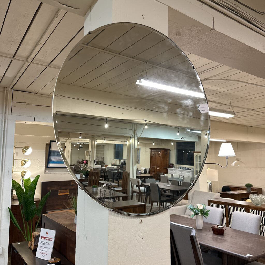 Large round mirror reflecting a room with tables, chairs, and decor.