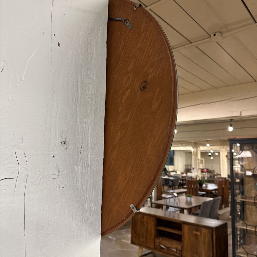 Wooden half-circle mirror leaning against a white wall in a room with tables and chairs.