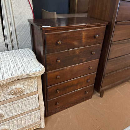 Wooden dresser with multiple drawers next to a wicker stool on a brown floor.