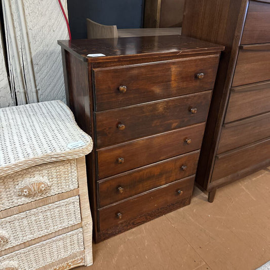 Wooden dresser with multiple drawers next to a wicker stool on a brown floor.