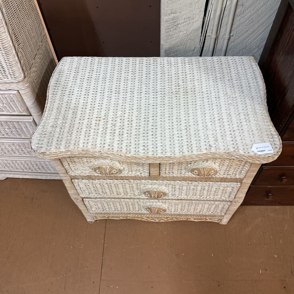 Wicker side table with two drawers on a brown floor.