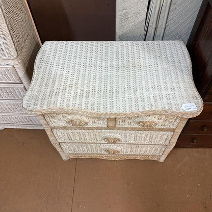 Wicker side table with two drawers on a brown floor.