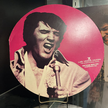 Memorabilia with a cutout of a person holding a microphone against a pink background, featuring the Las Vegas Hilton logo.