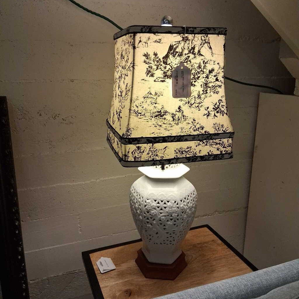 Lamp with decorative shade on a wooden surface against a textured wall.