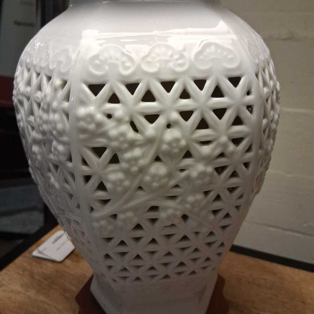 White ceramic vase with intricate lattice design on a wooden surface.