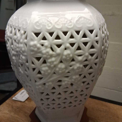 White ceramic vase with intricate lattice design on a wooden surface.