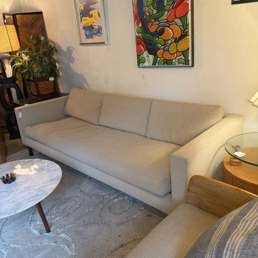 Beige sofa in a living room with a colorful abstract painting on the wall.