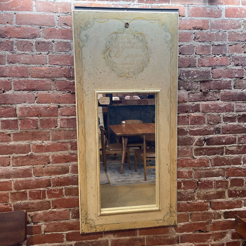 yellow wooden framed mirror with french script on top hanging on a brick wall