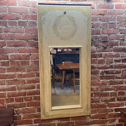 yellow wooden framed mirror with french script on top hanging on a brick wall