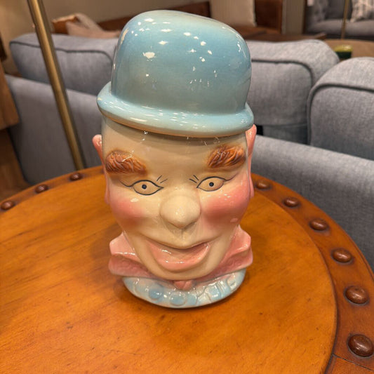 Vase shaped like a person's head with a light blue top hat on a wooden table.