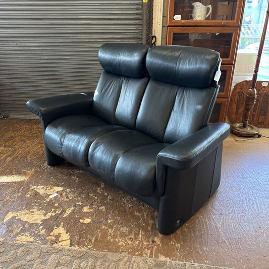 Black leather sofa in a room with a wooden floor and a cabinet in the background.