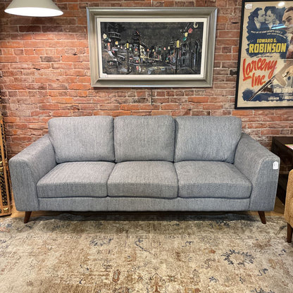 Gray sofa in a room with a brick wall, framed picture, and vintage poster.
