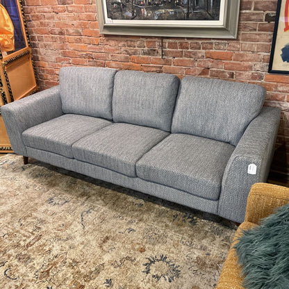 Gray sofa in a room with a brick wall and framed pictures.
