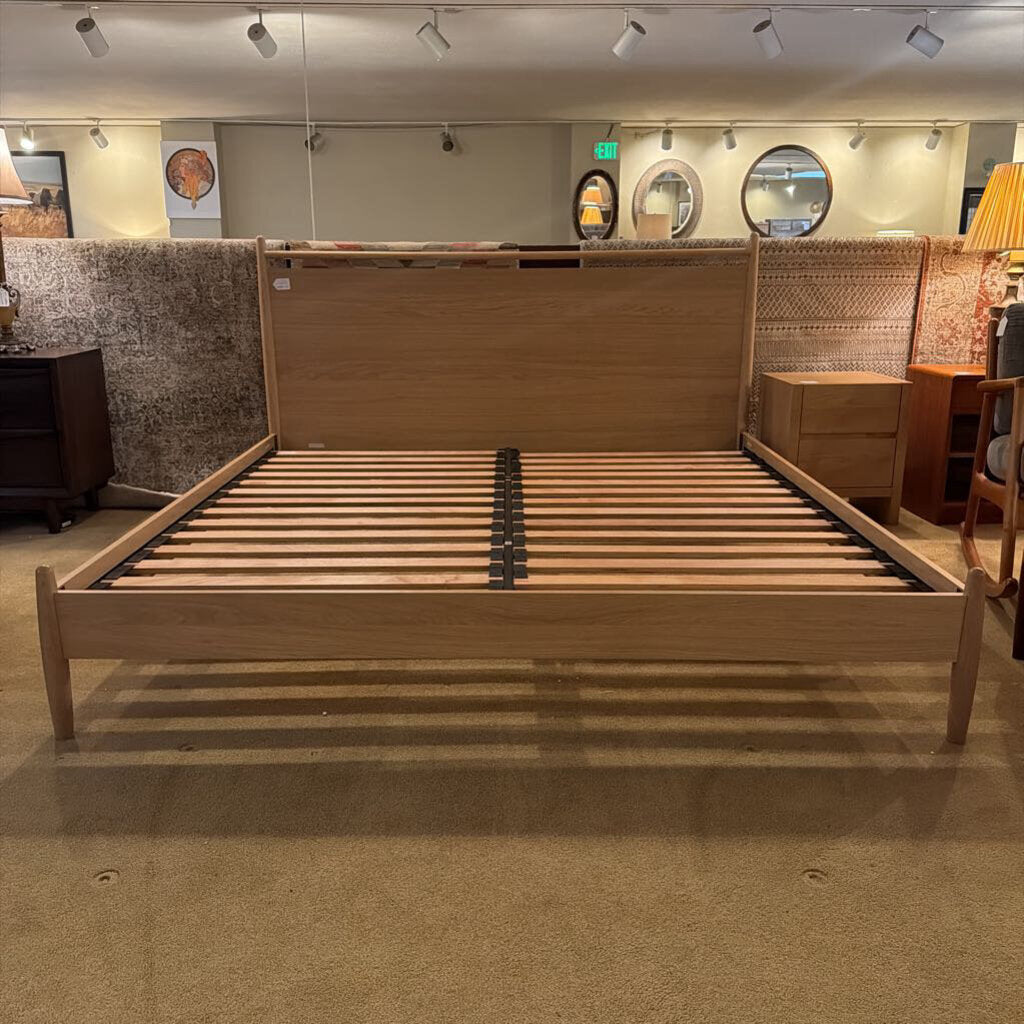Wooden bed frame in a showroom setting with various decor items in the background.