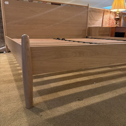 Wooden bed frame on a carpeted floor with a lamp in the background