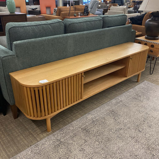 Wooden TV stand in front of a green sofa in a living room setting