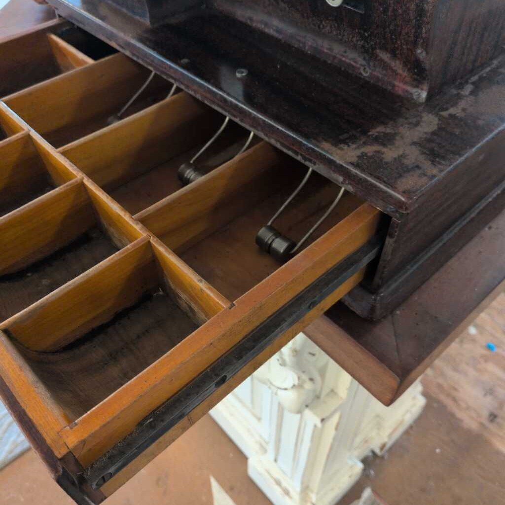 Vintage cash register with open wooden drawer on a wooden floor.