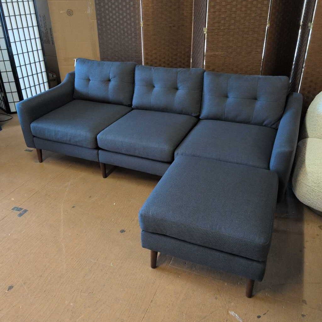 Blue sectional sofa in a room with a textured wall and wooden floor.
