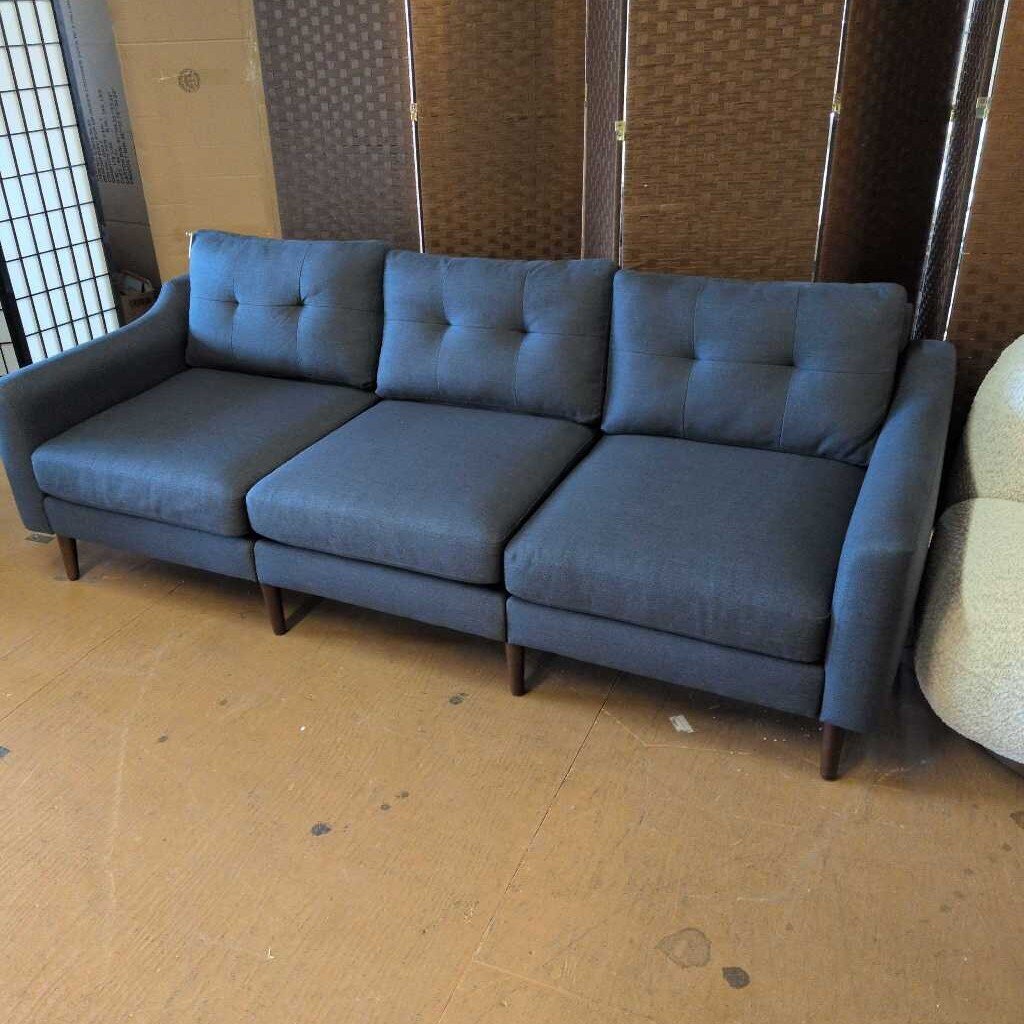 Blue sectional sofa in a room with a textured wall and wooden floor.