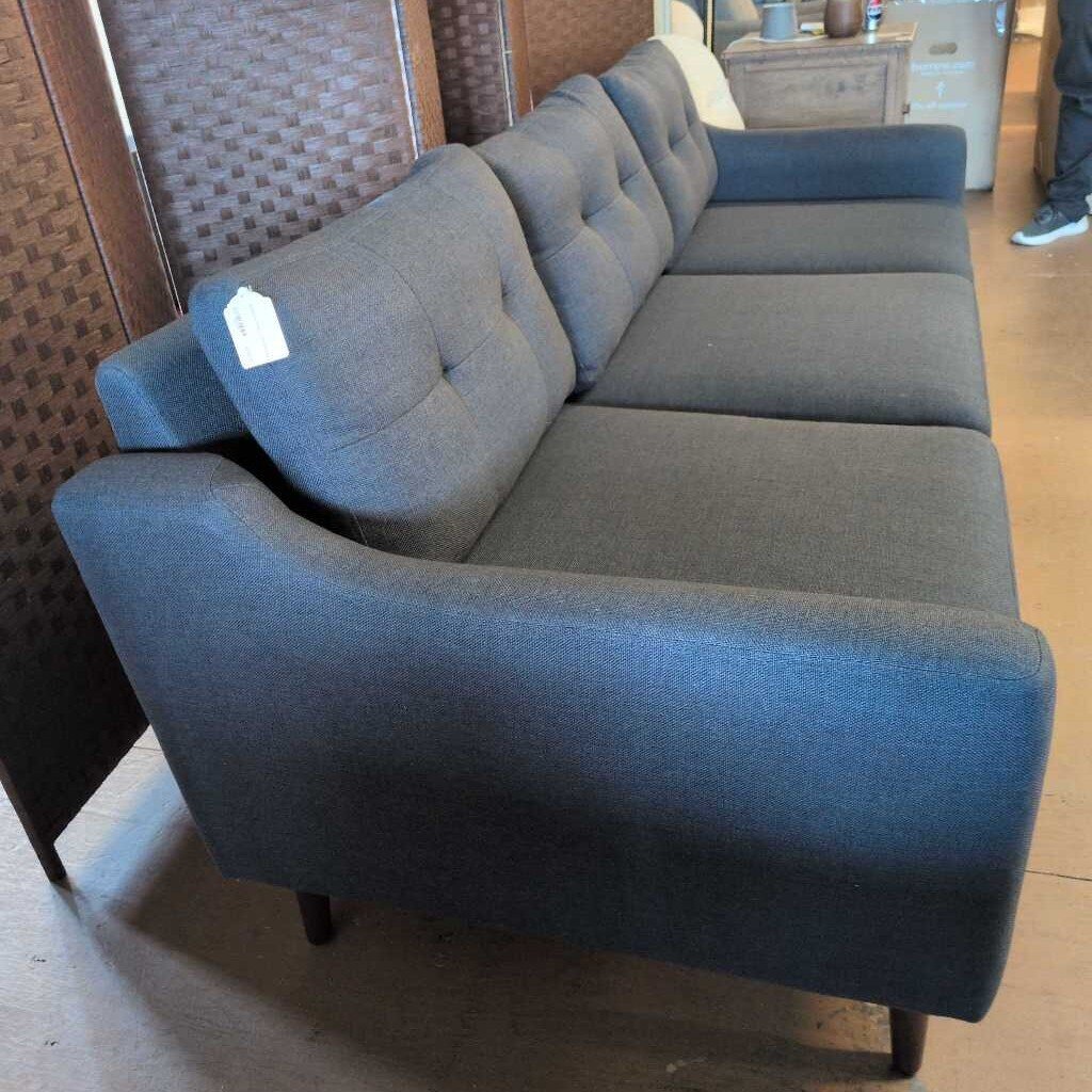 Gray sectional sofa in a room with wooden flooring and a wall.