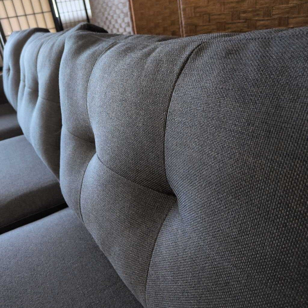 Gray upholstered headboard of a bed with a textured fabric finish.