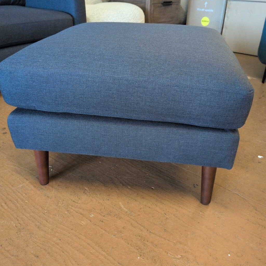 Blue ottoman on a wooden floor with furniture in the background