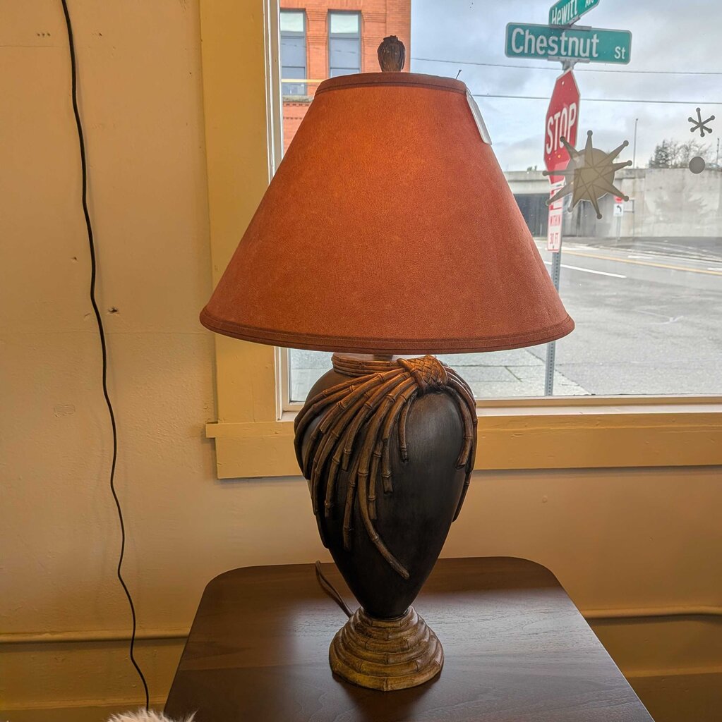 Decorative lamp with a brown shade on a table next to a window with street signs.