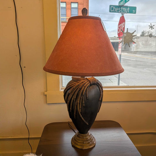 Decorative lamp with a brown shade on a table next to a window with street signs.