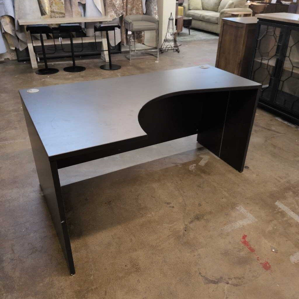 Black L-shaped desk in a showroom setting with furniture in the background