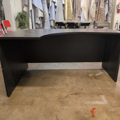 Large black L-shaped desk in a room with clothing racks in the background.